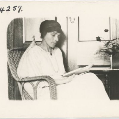 woman sits in a wicker chair reading a book